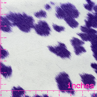 The printed violet cow print fabric is a striking and playful textile featuring a whimsical interpretation of traditional cow spots in various shades of violet, from deep purple to soft lavender. The irregularly shaped spots are set against a contrasting white or light cream background, making the pattern stand out vividly